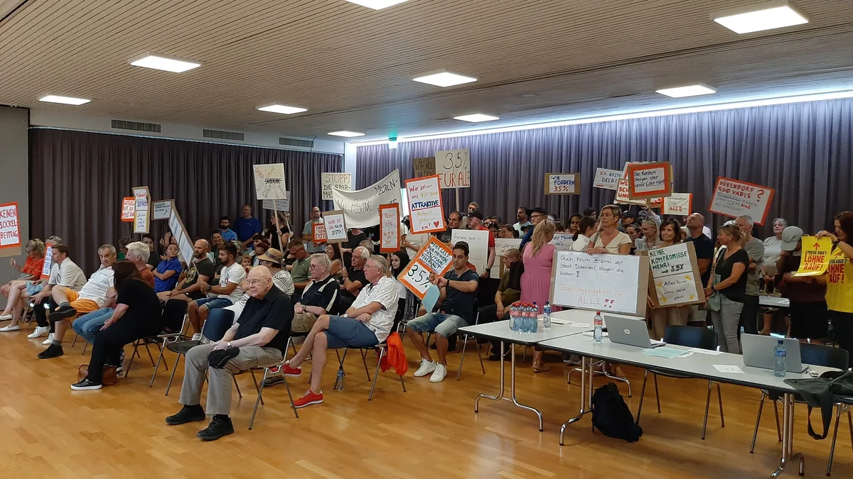 Eine Menschenmenge mit Protestplakaten in einem Saal. 